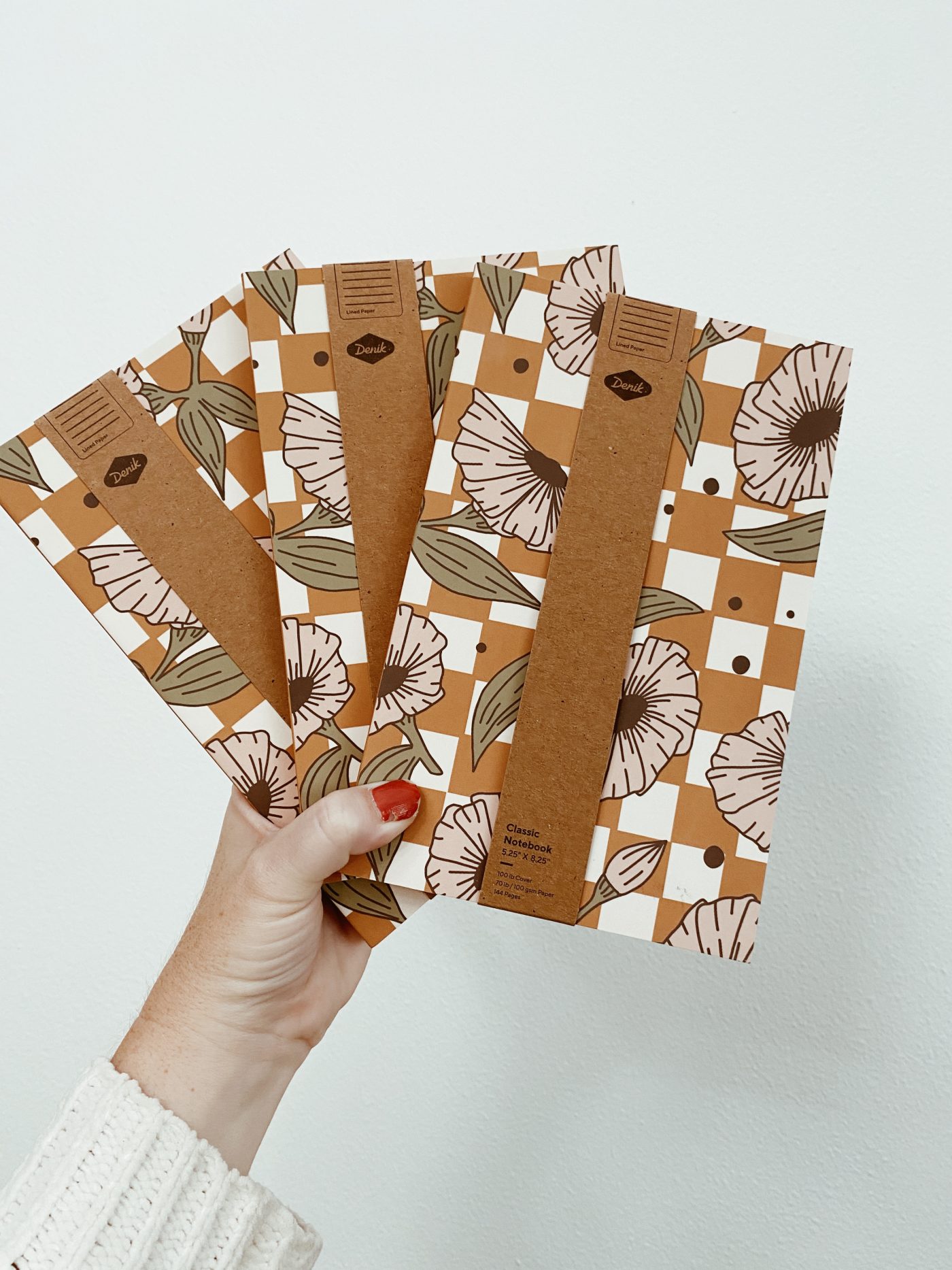 Hand holding floral patterned notebooks against white wall