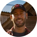 Smiling man in baseball cap outdoors near wooden structure