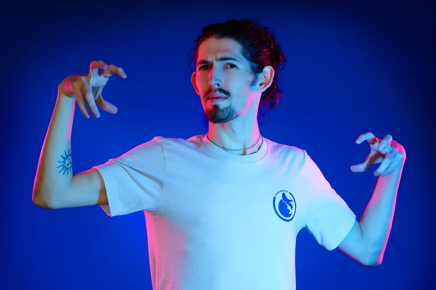 Man posing with expressive hands, blue and pink lighting.