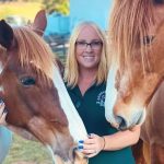Smiling woman with two horses at farm.